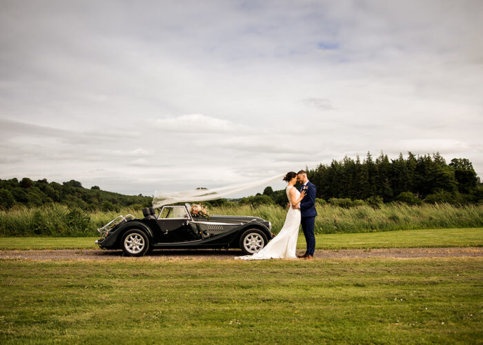 Bride and Groom standing beside vintage car