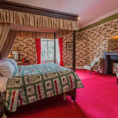 A four poster bed in a room with horse riders on wallpaper