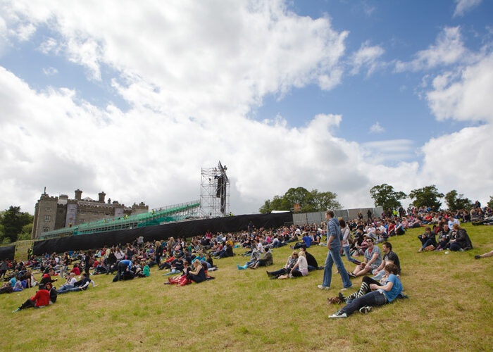 a crowd sitting on grass at concert Slane Castle in the background