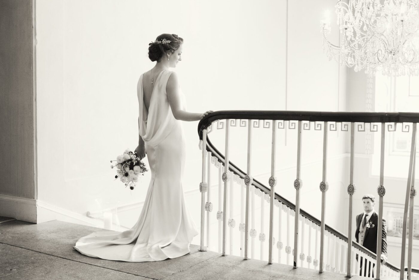 A bride stanging at the top of the stairs groom waiting below