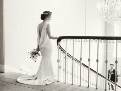 A bride stanging at the top of the stairs groom waiting below