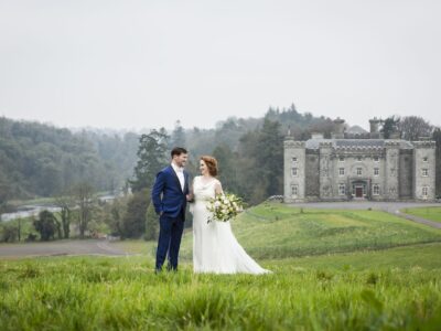 A wedding couple standing on a hill with Slane Castle in the background